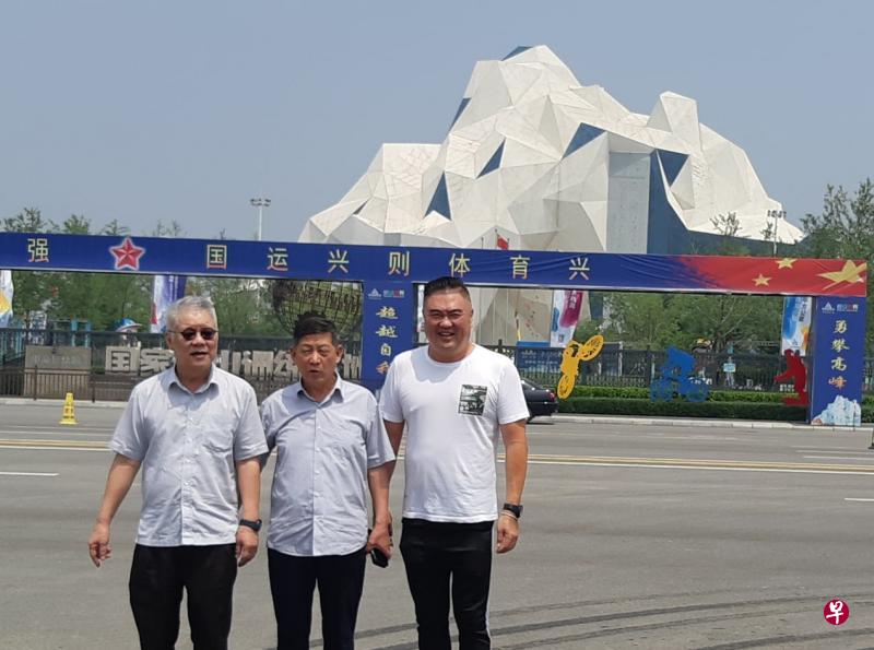 　陈积光（右起）、赵文泉和朱峙安背后是刚落成的号称世界第一大的人工攀岩岩壁。（受访者提供）