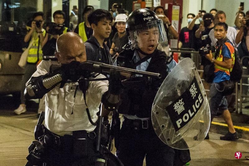 刘泽基（左）和另一名警员7月30日在葵涌警署外被反修例示威者围攻，他两度举起散弹枪指向示威者，以示警告。（法新社）