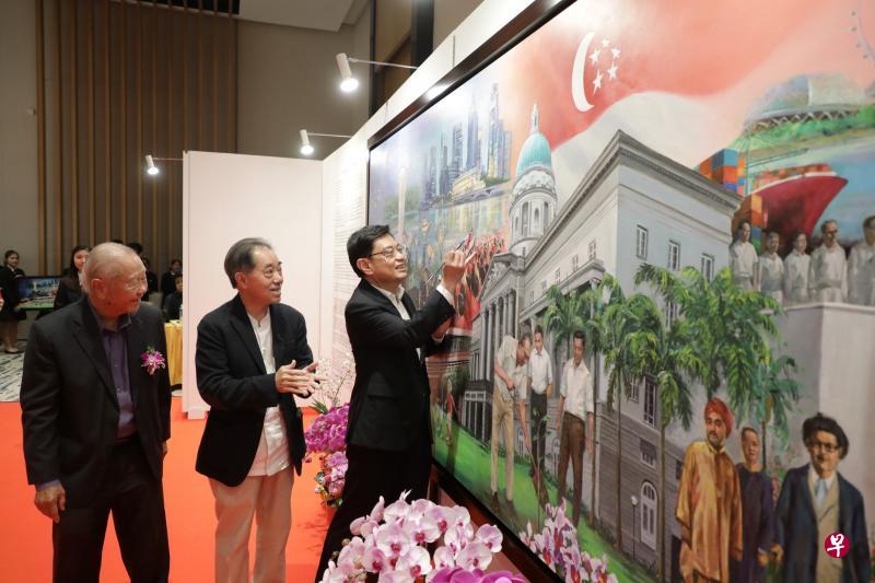 副总理兼财政部长王瑞杰（右一）昨天在新加坡艺术协会会长赵振强（中）和顾问何家良博士（左一）的见证下，为老中青三代画家集体创作的画作“我们的故事”添上一笔。（林国明摄）