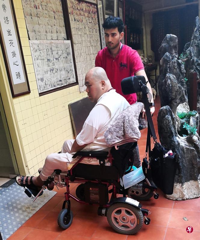 传文法师去年6月中风后需轮椅代步，图中的印度籍男看护负责推着他出入。（饶进礼摄）