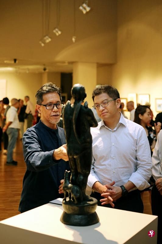 林序毅（左）向本届潮人艺术展主宾——义安公司总理张绵耀，介绍他的铸铜人物作品。（龙国雄摄）