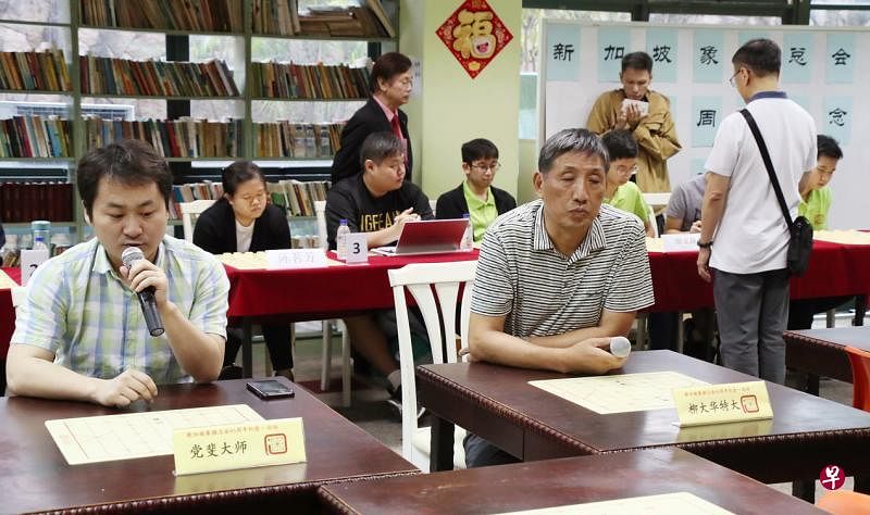 柳大华（前右）与党斐（前左）闭目与背后六名年轻棋手对弈，左后方站立观察赛事者为象总会长林关浩。（陈来福摄）