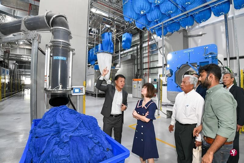 八百控股总裁李清财（左一）向卫生部兼环境及水源部高级政务部长许连碹博士（左二）讲解抽吸系统可直接将衣物抽吸装入工业烘干机器里。（八百控股提供）