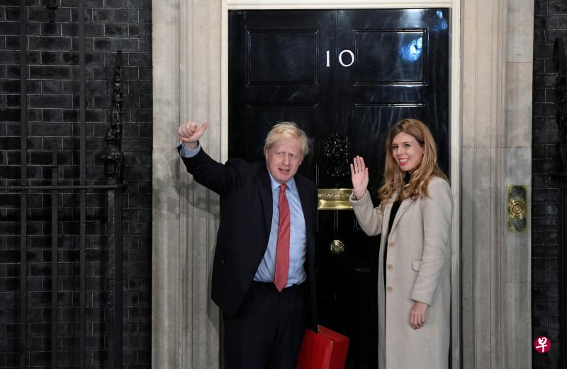 英国首相约翰逊周五在大选开票势头一路挺进之后，同女伴西蒙斯回到伦敦唐宁街10号首相官邸，进门前向媒体竖起大拇指。（路透社）