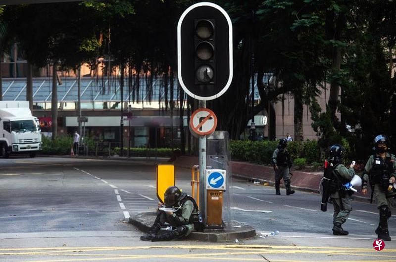 香港社会抗争期间，一名防暴警员因职务在身，靠在遭破坏的交通灯下席地吃饭盒。（取自香港警务处面簿）