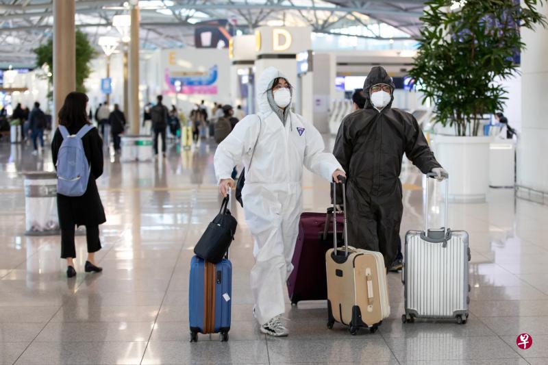 韩国冠病疫情严重，进出仁川机场的旅客提高警惕，图中这两名可说做足防护措施，除了脸戴口罩，还穿起防护服。（彭博社）