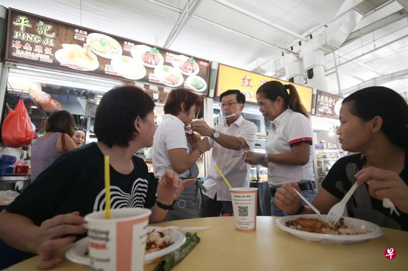 东海岸集选区议员李奕贤（中）派口罩给熟食中心摊贩，鼓励小贩采取最佳作业方式，也提高民众对熟食中心卫生水平的信心。（陈渊庄摄）
