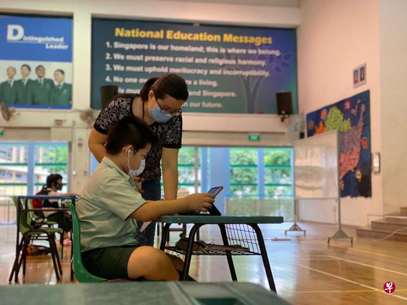 华苑小学三年级生石俊豪因父母都从事必要服务行业，他过去四周可以继续到学校，在教师的引导下进行学习。图为学校教育协作人员林婧煊（站立者）指导石俊豪使用学校提供的平板电脑。（华苑小学提供）