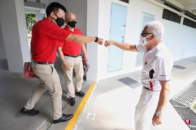 民主党候选人江伟贤（左起）、方月光昨天走访蔡厝港弯组屋时遇见行动党基层人员，疫情中巧遇，双方保持安全距离，江伟贤与对方击拳问候。（李健玮摄）