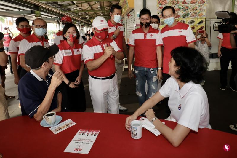 新加坡前进党秘书长陈清木医生（拱手者）为该党的丹戎巴葛集选区候选人孙俊伟（后排左起）、阿巴斯·卡斯马尼和刘韦伶助选，他在走访红山景熟食中心和巴刹时巧遇人民行动党候选人祖安清心（坐者右）。（陈斌勤摄）