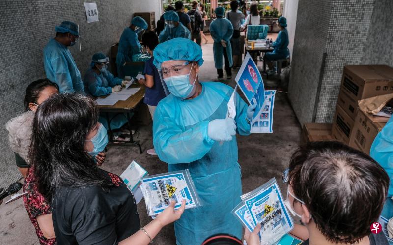 港府扩大冠病社区检测计划，工作人员昨天到九龙黄大仙慈爱苑向居民派发咽拭子采样套装和登记表格，并预计于今天收回样本进行测试。图为工作人员向居民简介咽拭子采样流程及注意事项。（中通社）