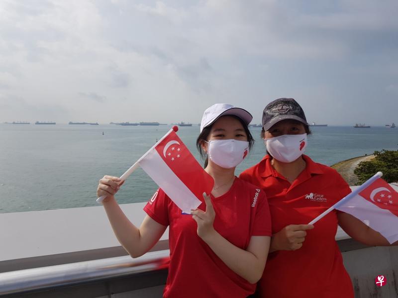 舰队敬礼仪式很有意义，我朋友正好在其中一艘军舰上服务，她和我介绍海军在疫情期间如何保护新加坡海域，确保海运畅通。朋友也和我解释仪式的意义，我希望通过行动来感谢海军，因此过来滨海堤坝为他们加油打气。——蔡爱丝（右，50岁，自雇人士）与林嘉嘉（21岁，学生）
