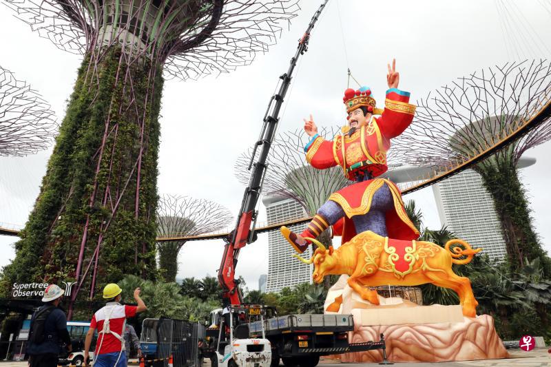 迈入第35个年头的春到河畔今年以“牛转乾坤，春暖花开”为主题，活动将从2月10日至16日，在全新场地滨海湾花园举行。工作人员这几天正赶工组装灯饰，包括这尊18米高、摆出胜利手势的财神爷。（邝启聪摄）