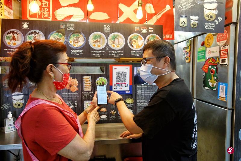 麦士威熟食中心的小贩对电子付款有疑问，都会找Tonkotsu Ramen的老板陈福顺（右）解答和帮忙，陈福顺也非常乐意协助其他小贩熟悉电子付款。（特约陈福洲摄）