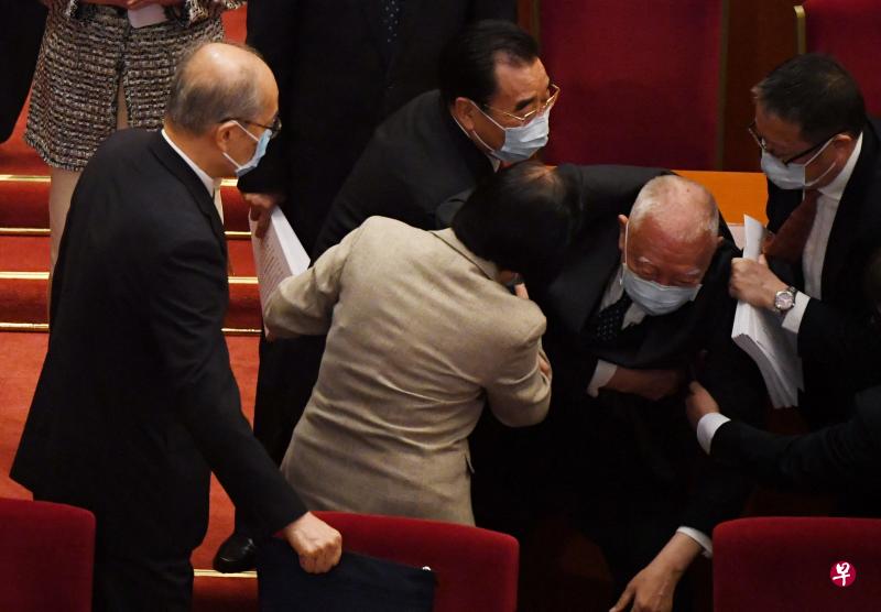 董建华离开座位时突然跌倒，旁边的人连忙上前搀扶。（法新社）