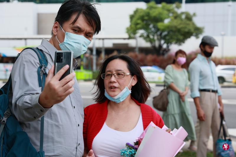 反疫苗接种群组“Healing the Divide”创办人许淑慈（左二）获准保释，约十名支持者到警署外接她，丈夫（左一）帮她做直播。（潘丰源摄） 