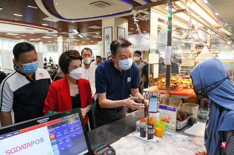 贸工部兼文化、社区及青年部政务部长刘燕玲（左二）、消协主席杨益财（左三）和长城集团主席郭观华（左一）向摊贩解释“省钱之友”的功能。（卓祾祎摄） 