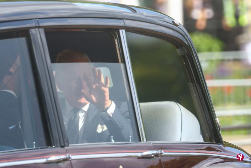 英国国王查尔斯三世18日乘车到白金汉宫，透过车窗向民众挥手致意。（路透社） 