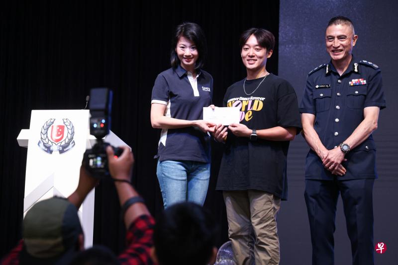 电单车骑士陈庆洲（中）展现出良好的公路安全意识，从内政部兼社会及家庭发展部政务部长孙雪玲（左）的手中接过奖品。（李健玮摄） 
