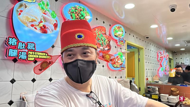 杂菜饭摊位助手陈先生变身“财神爷”，戴上财神帽为食客添饭夹菜。 （曾美玲摄） 