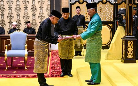 马来西亚第10任首相安华（左）星期四在国家王宫宣誓就任。他从国家元首苏丹阿都拉（右）手中接过首相委任状和宣誓书后，宣读宣誓词并签名，完成就职仪式。（法新社）