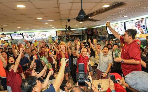 黄梨是尚达曼的竞选标志，众多支持者在选举官宣布尚达曼当选总统时，在咖啡店高举黄梨欢呼。许多支持者喝黄梨汁、吃黄梨庆祝，并跟自备的黄梨拍照留念。（吴先邦摄）