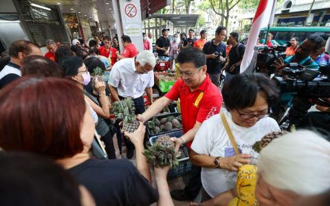 政治观察家认为，尚达曼选择黄梨作为竞选标志，堪称“神来之笔”。图为裕廊凤山寺的理事（红衣）在尚达曼到达曼裕廊巴刹及熟食中心答谢选民之前，分发黄梨给公众。（陈渊庄摄）