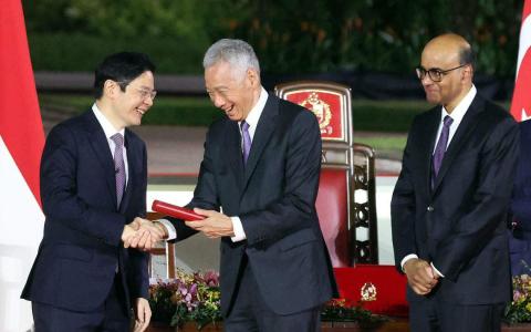 留在内阁并出任国务资政的李显龙（中）在总统府举行的宣誓就职仪式上，从尚达曼总统（右）手中接过委任状后，转身同总理兼财政部长黄循财握手致意。（何家俊摄）
