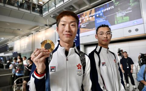 香港击剑运动员张家朗（左）星期五（8月2日）上午从法国巴黎乘机返回香港，大批传媒和市民到机场迎接。图为张家朗手持金牌返港。（中新社）
