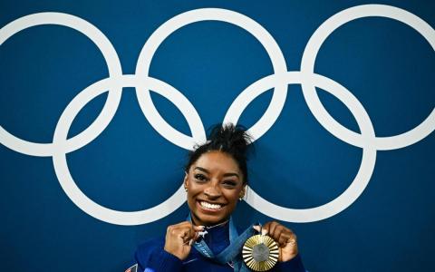 西蒙妮在奥运五环前，兴奋地展示赢得的金牌和她戴着的山羊（英语GOAT，是“历代最伟大的简称”）项链。这条项链镶有多达546颗钻石。（法新社）