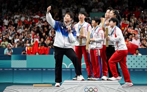 获得混双乒乓球银牌的朝鲜选手李正植（左二）和金琴英（左三）与获得铜牌的韩国选手林仲勋（左一）和申裕斌（右二），以及获得金牌的中国选手王楚钦（右三）和孙颖莎（右一）一起自拍。尽管这一时刻普遍被视为本届奥运会世界大同的经典画面，但却可能使朝鲜选手陷入麻烦。（法新社）