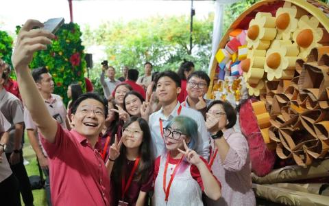 黄循财总理（红衣者）在总统府举行的新春园游会上，与基层领袖自拍合照。在他们身后的，是以再循环材料制成的年饼拼盘造型。（谢智扬摄）