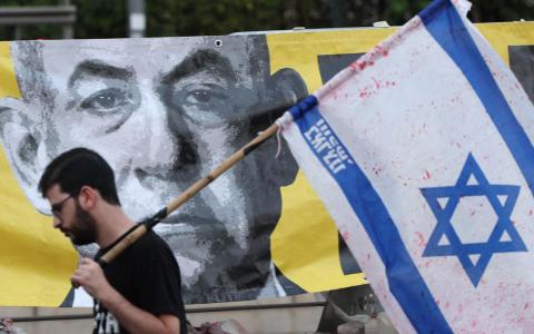 6月7日，一名示威者手持以色列国旗，走过一幅以色列总理内坦亚胡的肖像画。（法新社）