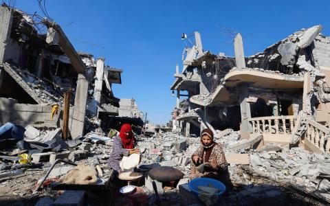 星期四以哈休战期间，加沙南部城市汗尤尼斯的两名巴勒斯坦妇女坐在户外烘烤面包，她们周围的房子在以色列空袭中被摧毁。（路透社）