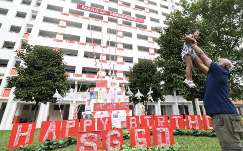 蔡厝港53街第702座组屋前悬挂着一条条印有新加坡地标与祝福语的横幅，层层叠叠铺展开来，宛如一座精心打造的多层生日蛋糕，不仅为国庆增添喜庆气氛，也象征新加坡60年来一步一脚印、稳扎稳打的发展历程。沉浸在国庆热烈喜庆的氛围中，老少居民在熟悉的社区漫步赏景，让年幼的一代在成长的地方，更深刻地认识这片属于他们的家园。（陈斌勤摄）