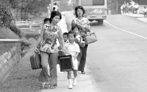 1976年的小学开学日，穿着整齐校服的小学生提着小黑板，在家长陪同下上学去。（档案照片）