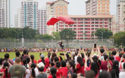 红狮跳伞队的队员们带着红白降落伞在草场安全着陆，现场观众也先后响起热烈掌声和喝彩迎接他们。（谢智扬摄）