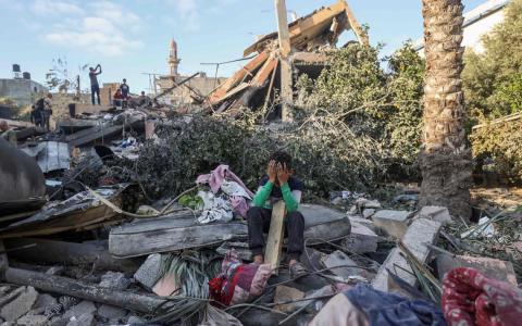 加沙当局说，以色列最新空袭造成逾百人死亡，周三在加沙中部努塞拉特，一名男童掩面坐在被炸毁的房屋废墟中。（法新社）