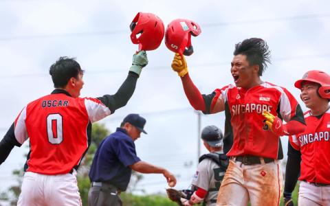 余安（红衣中）在比赛中打出三分全垒打，帮助我国扩大优势后，兴奋地与队友郑丁铨（左）互碰棒球头盔庆祝。（新加坡全国奥理会提供）
