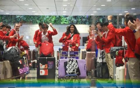 结束本届东运会后，我国男子400米栏冠军郭俊杰（中左）和女子100米、200米双冠王珊蒂（中右）在教练库尼亚（左三）和随行职员的列队欢呼下，推着行李缓缓走出抵达厅。（陈渊庄摄）