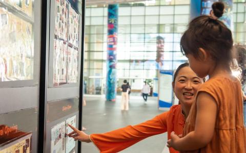 梦想板创始人林美岄（面向镜头）和一个走进“梦想板”展区的小朋友，分享展场上人们描绘的梦想与对国家发展的期望。（新加坡政民合作署提供）