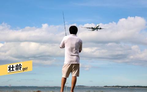 海岸边，一名垂钓者静静地等待鱼儿上钩，飞机从他身旁低空掠过。（关俊威摄）