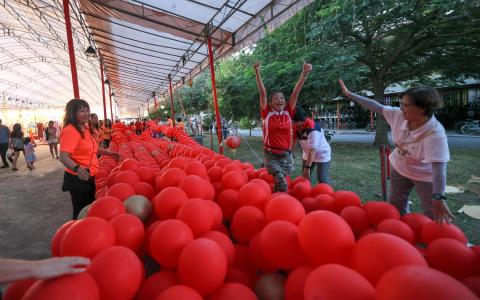 义顺中区公民咨询委员会副主席洪宝妹（右二，身穿红衣）经常带领气球创作兴趣小组为社区活动做布置，这次也与义工为新春亮灯活动制作约150米长的气球鞭炮。（张俊杰摄）