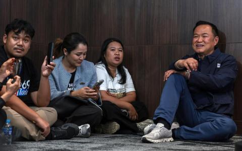 星期天开票夜，看守首相阿努廷（右一）坐在地上接受记者采访，显示他不拘小节的一面。（路透社）