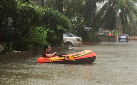 孟买近日暴雨肆虐，多条道路被淹，一名男子在积水中划充气艇移动。（路透社）