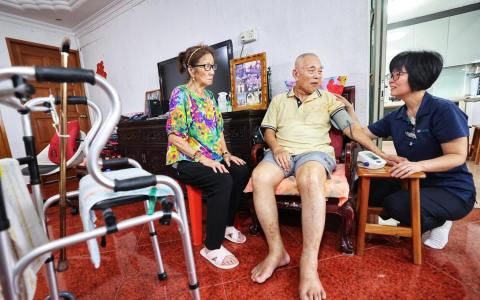 邱德拔医院高级护士林姹婷（右一）说，杨钟佳（中）行动不便，家中又只有年迈妻子马振菊（左一）照顾他，太和观看护员全天上门照护，大大减轻了妻子的负担。（萧紫薇摄）