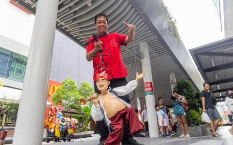 平日中午，在大巴窑市镇中心的街道上，从事人偶艺术表演逾60年的温忠全顶着烈日，操控手中的人偶。（吴先邦摄）