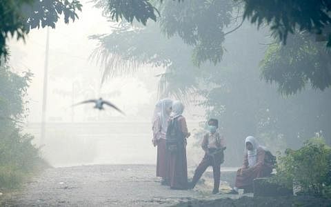 ▲亚齐省西岸港市米拉务昨日烟霾笼罩，学生们戴口罩在路旁等候搭巴士上学。（法新社）