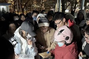 2023年11月，“鹅腿阿姨”在北京大学门外，向学生分发他们提前在微信预订的烧烤“鹅腿”。（北青报）