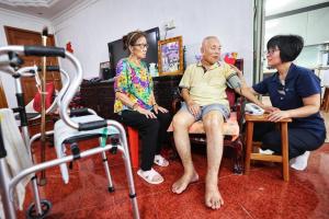 邱德拔医院高级护士林姹婷（右一）说，杨钟佳（中）行动不便，家中又只有年迈妻子马振菊（左一）照顾他，太和观看护员全天上门照护，大大减轻了妻子的负担。（萧紫薇摄）